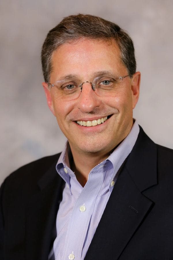 Dan James, founding partner, in a dark jacket and open-collared shirt against a studio backdrop.